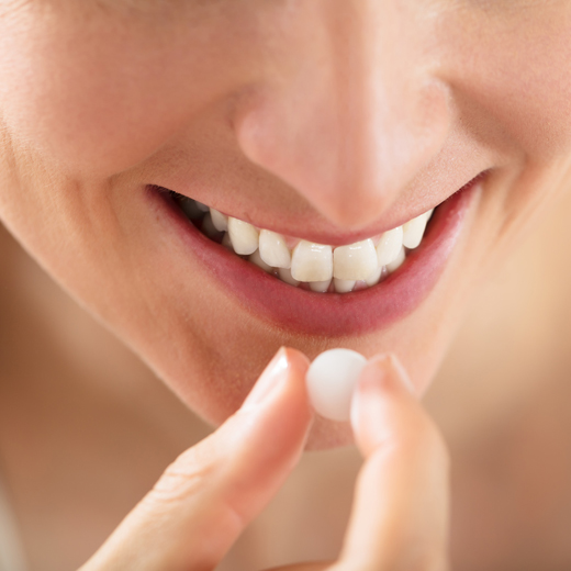 Close-up Of Female Hands Putting One White Round Pill On Tongue